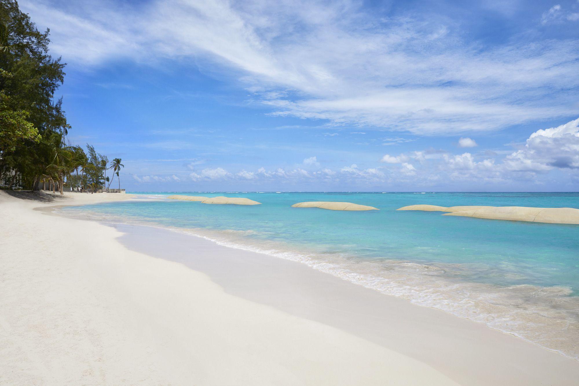 Impressive Punta Cana Exterior foto The photo showcases a beautiful beach scene. In the foreground, there is soft, white sand leading to clear, turquoise waters. Gentle waves lap at the shore. In the background, palm trees can be seen lining the beach, and the sky is bright with a few 