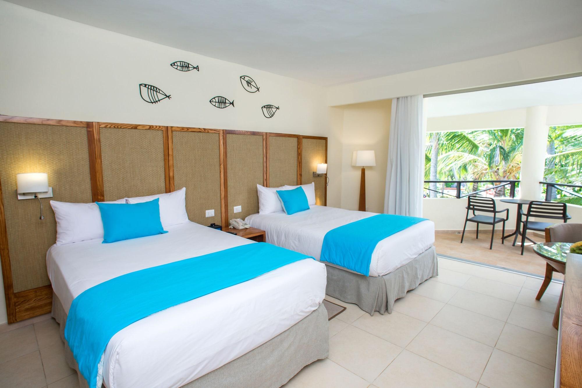 Impressive Punta Cana Exterior foto The photo shows a hotel room featuring two beds with white linens and bright turquoise decorative elements. The walls are light-colored, and there's a decorative pattern of fish above the beds. The room has a lamp beside one of the beds and a spaciou