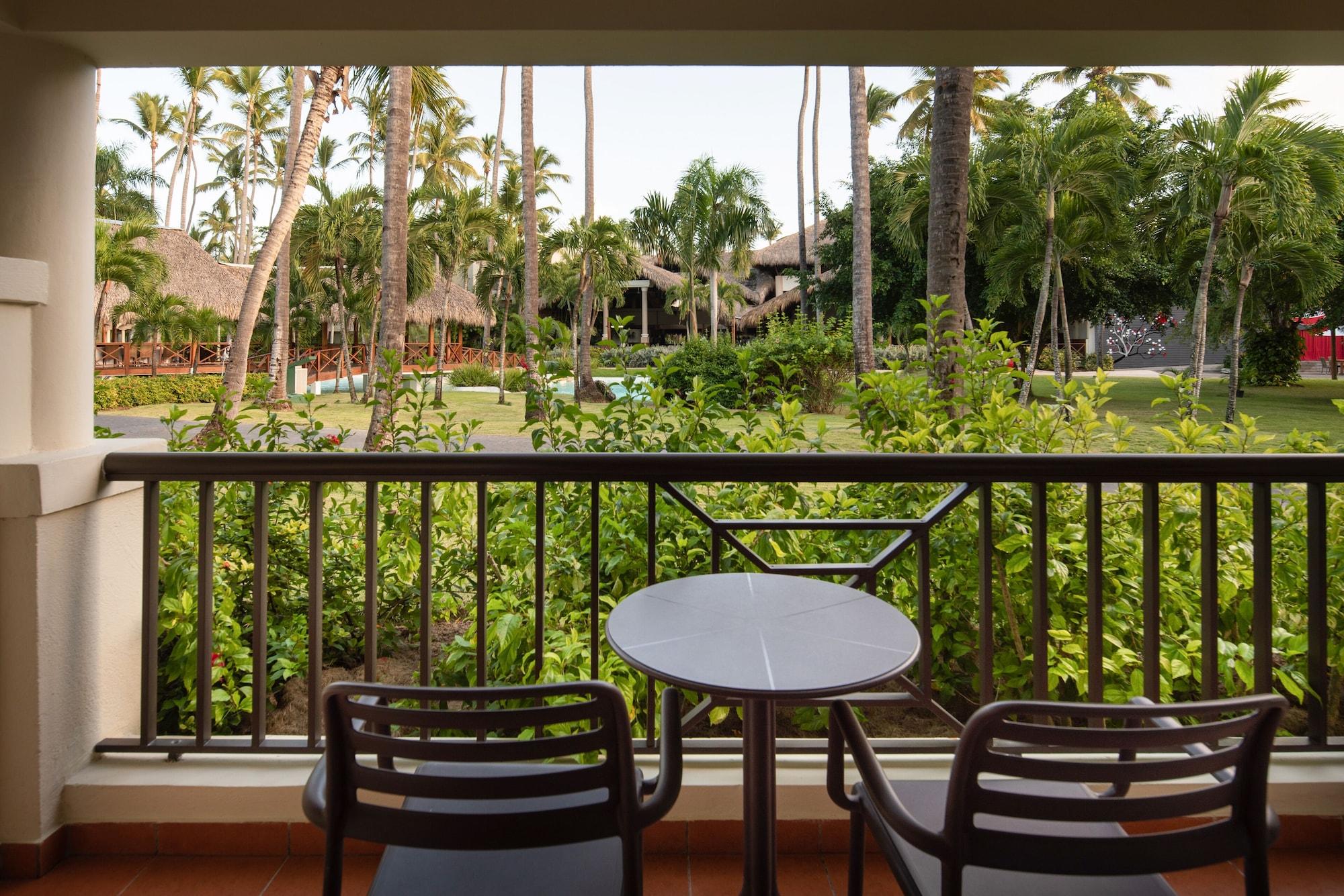 Impressive Punta Cana Exterior foto The photo shows a view from a balcony with two black chairs and a small round table. In the background, there is a lush green landscape filled with palm trees and other vegetation, suggesting a tropical setting. The area appears well-maintained, with