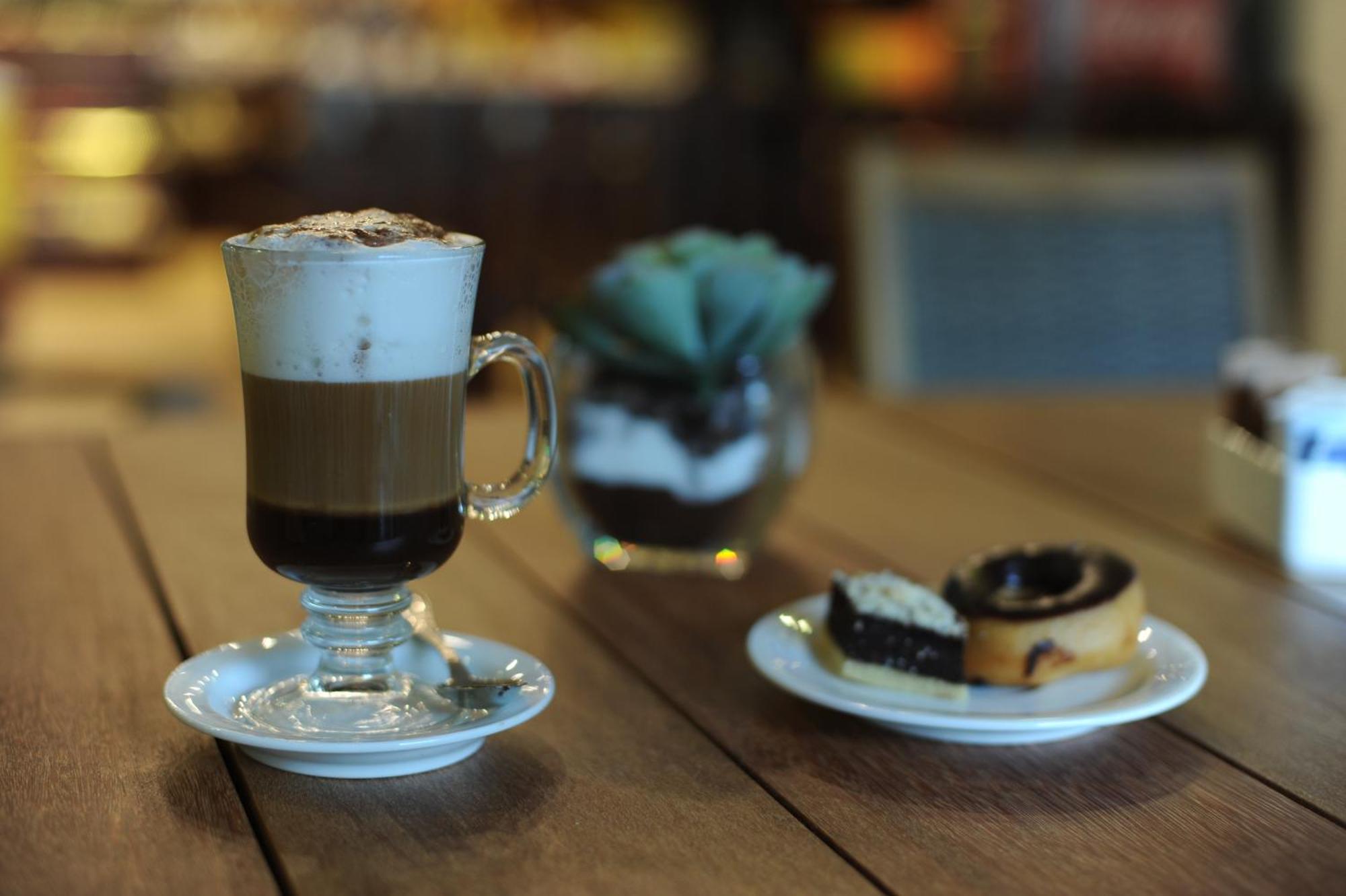 Impressive Punta Cana Exterior foto The photo shows a glass of layered coffee topped with foam and possibly cocoa powder, presented on a small white plate. Beside the coffee, there is a plate with two types of pastries: one appears to be a swirl-shaped pastry, likely cinnamon or chocol