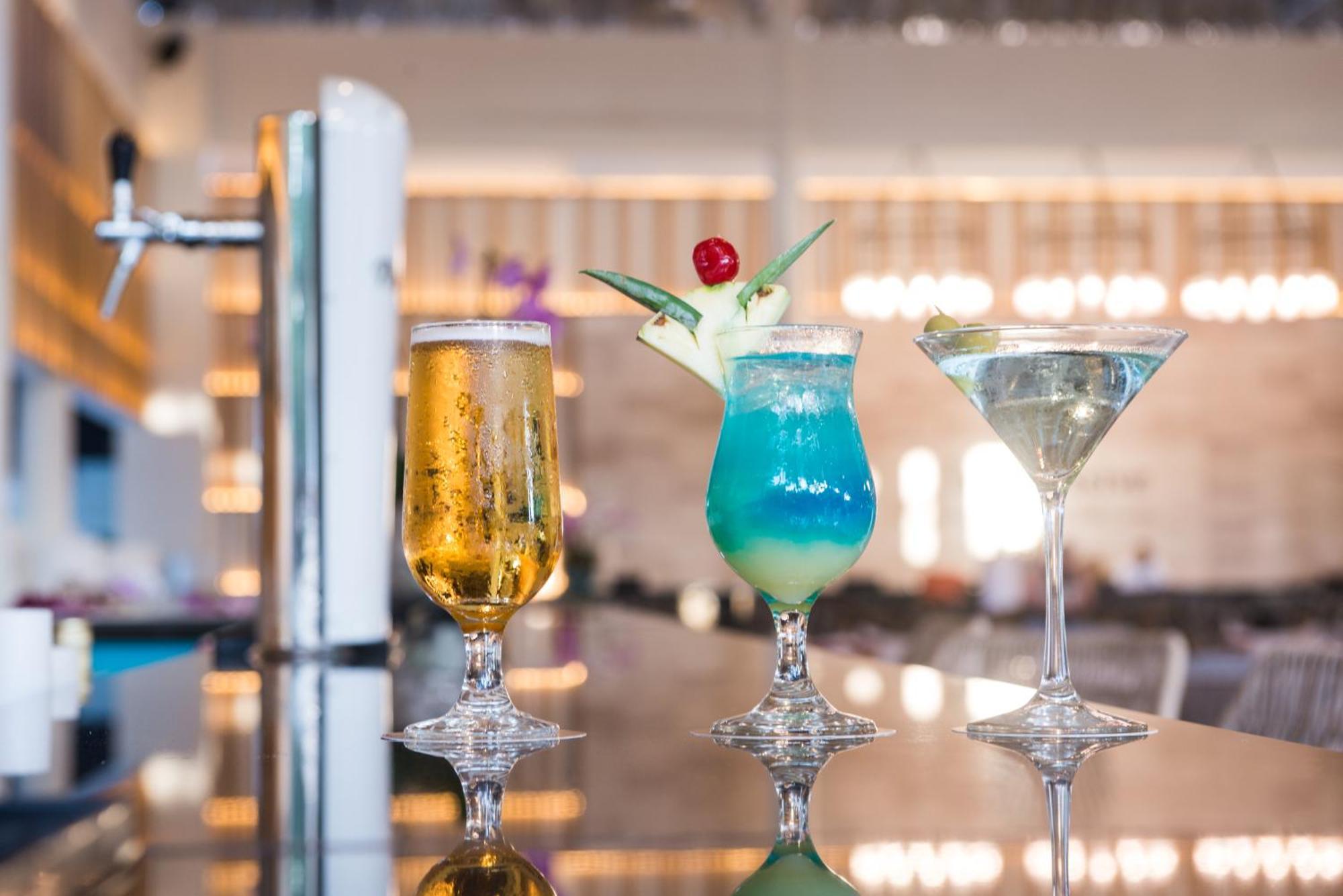 Impressive Punta Cana Exterior foto The photo features three different cocktails presented on a shiny surface. 

1. On the left, there is a tall glass of beer, which appears golden and bubbly, served in a flute-style glass.
2. In the center, a vibrant blue cocktail garnished with a pin